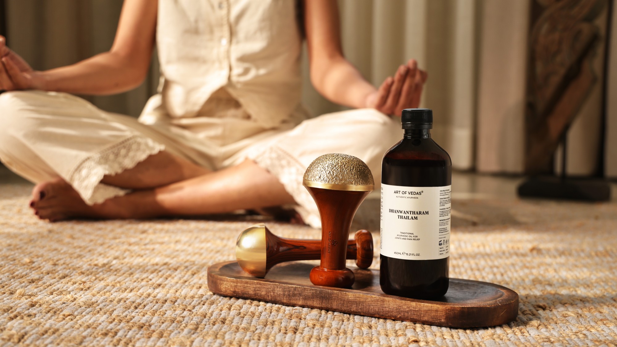 Art of Vedas Dhanwantharam Thailam in its PET bottle on a tray beside two Kansa wands